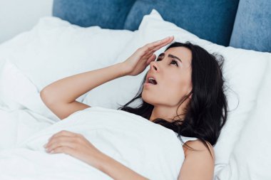 Shocked brunette woman lying in bed and looking up clipart