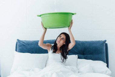 Frustrated woman holding basin during leak in bedroom clipart