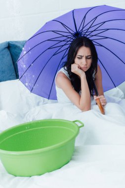 Sad girl holding purple umbrella during water leak in bedroom clipart