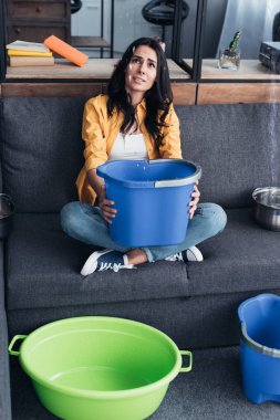 Upset woman with buckets and basin looking at leaking ceiling clipart
