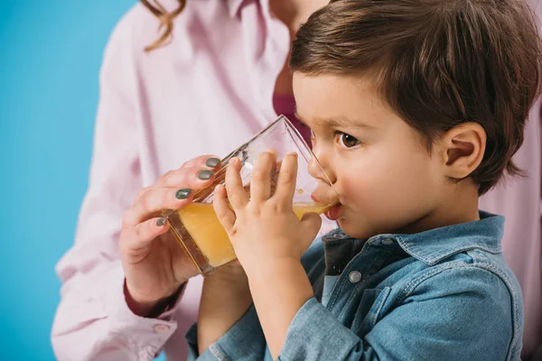 かわいい男の子とガラスを押しながら新鮮なオレンジ ジュースを飲む母親青に分離されたヘルプ — ストック写真