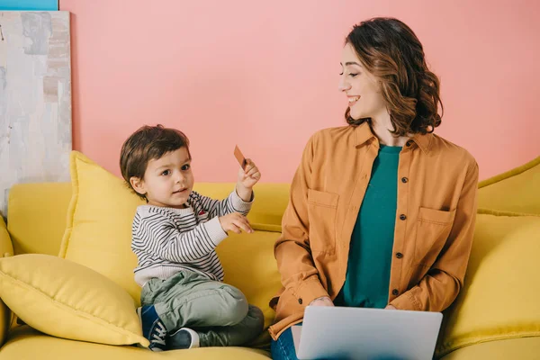 Cute Little Boy Holding Credit Card While Smiling Mother Using — Stock Photo, Image