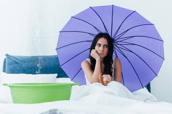 Грустная женщина, сидящая в постели с зонтиком во время повреждения водой
