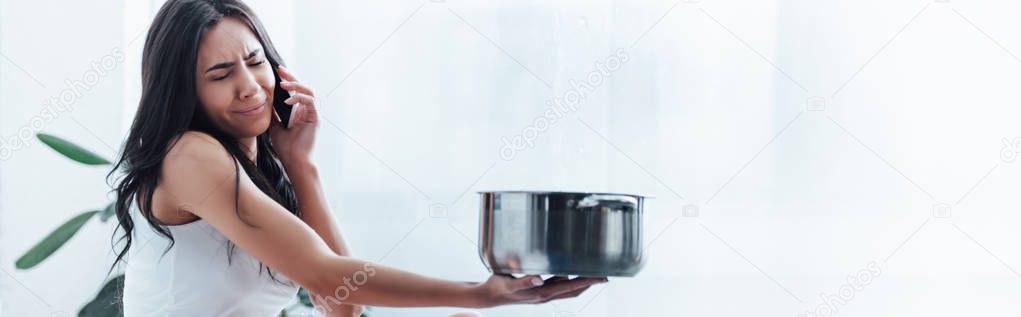 Upset woman talking on smartphone and holding steel pot