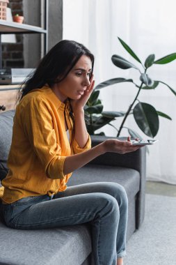 Kanepede oturan ve su tutan üzgün kız akıllı telefon zarar