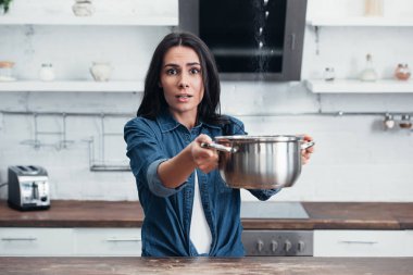 Amazed girl using steel pot during water leak in kitchen clipart