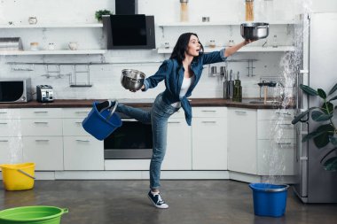 Full length view of shoked woman in jeans dealing with water leak in kitchen clipart