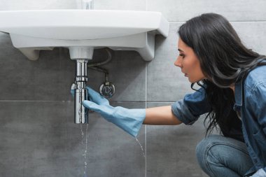 Brunette girl in rubber glove fixing pipe in bathroom clipart