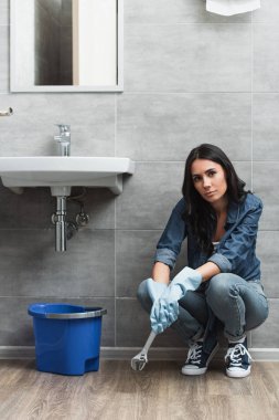 Tired girl with wrench sitting in bathroom clipart