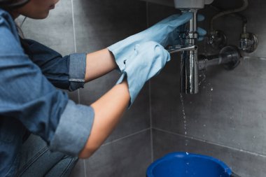 Partial view of woman in blue rubber gloves repairing pipe with wrench clipart