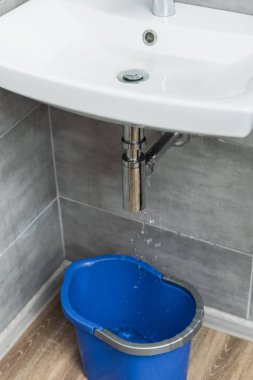 Hasarlı lavabo boru su damlaları ve mavi kova