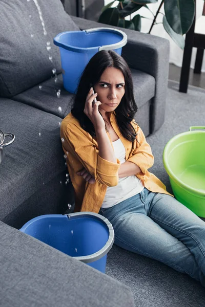 Uspet woman with smartphone looking at water drops in living room