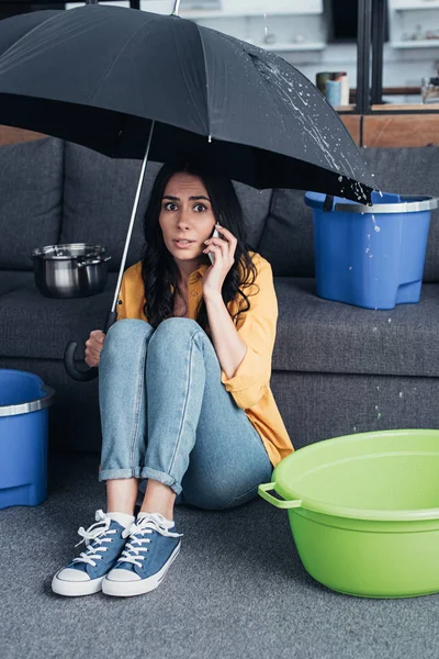 Verwirrte Frau Mit Smartphone Sitzt Unter Regenschirm Wohnzimmer — Stockfoto