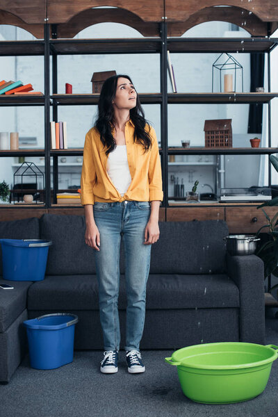 Full length view of sad brunette woman looking at leaking ceiling