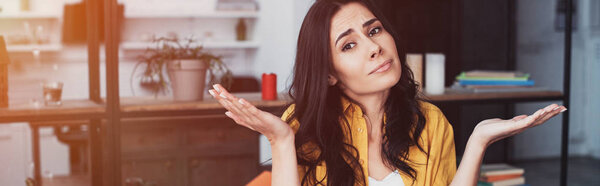 Confused brunette woman in yellow shirt standing with hands up