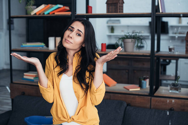 Confused woman standing with hands up under leaking ceiling in living room