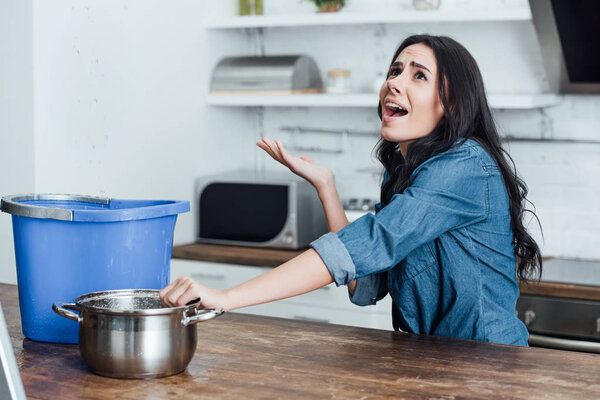Stressed brunette woman dealing with water damage in kitchen