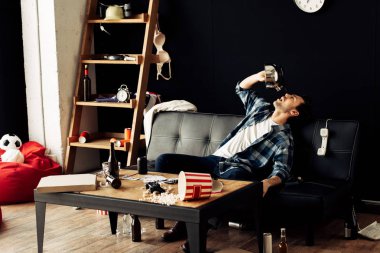 sarhoş adam dağınık oturma odasında kanepede otururken çaydanlık içme 