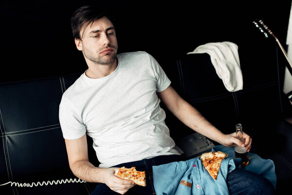 drunk man eating pizza and holding bottle in living room