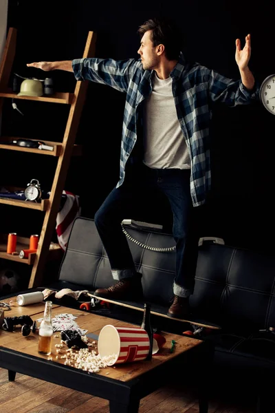 ソファのスケート ボードの上に立って 自宅でパーティー後身振りで示す陽気な男 — ストック写真