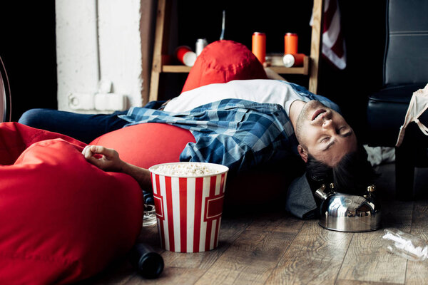 пьяный мужчина спит на фасолевом мешке рядом с попкорном
