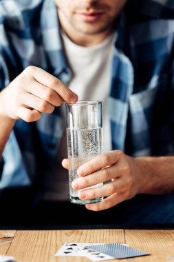 selective focus of man suffering from hangover holding aspirin and glass of water in hands clipart