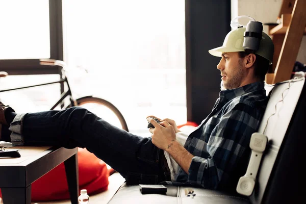 自宅でビデオ ゲームを遊んでビール ヘルメットでハンサムな男 — ストック写真