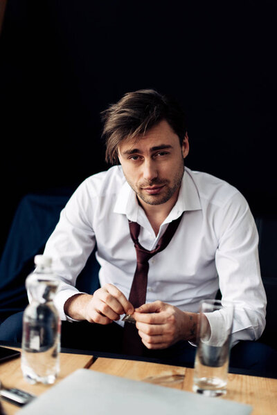 уставший бизнесмен держит таблетки в руках возле стакана воды после вечеринки
