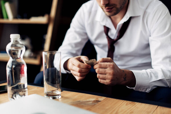 обрезанный вид бизнесмена, держащего таблетки в руках возле стакана воды
