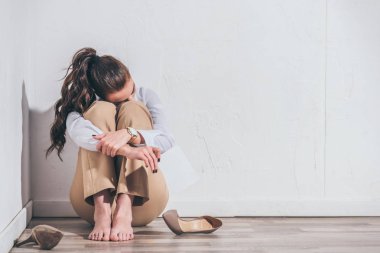 upset woman sitting on floor and holding photo near white wall at home, grieving disorder concept