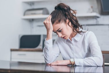 upset woman in white blouse sitting at table and crying in kitchen, grieving disorder concept clipart