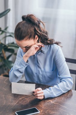 mavi bluz ile fotoğraf, smartphone ve evde, ağlayarak masada oturan üzgün kadın bozukluğu kavramı kederli