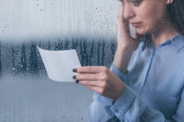 Kırpılan fotoğrafı tutarak ve yağmur damlaları ile pencereden ağlıyor yaslı kadın görünümünü