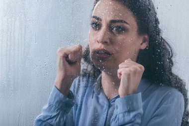 yağmur damlaları ile pencereden bakarak sıkışık yumruk ile güzel üzgün kadın