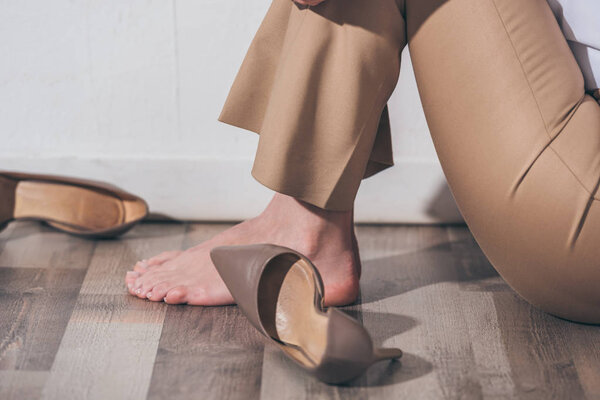 cropped view of woman in beige pants sitting on floor near white wall in room, grieving disorder concept