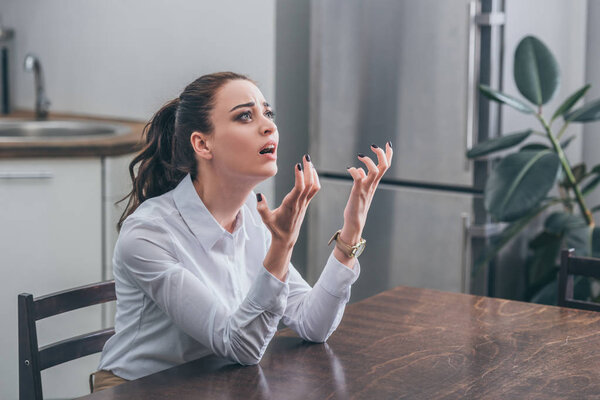 расстроена женщина в белой блузке, сидя за деревянным столом и молясь на кухне, горе концепции расстройства
