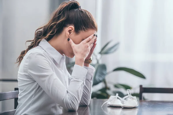 Upset Woman White Blouse Sitting Table Baby Shoes Covers Face — Stock Photo, Image