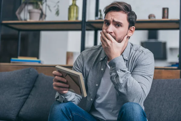 Man Sitting Grey Couch Holding Photo Frame Crying Home Grieving — Stock Photo, Image