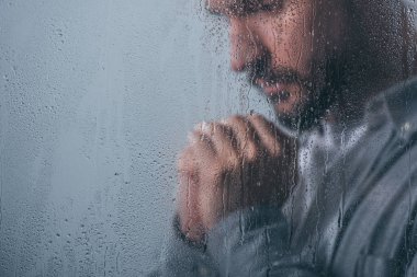 yağmur damlaları ve kopya alanı ile pencereden katlanmış ellerle üzgün adam
