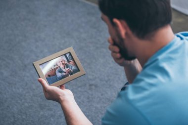 arkadan görünüşü yetişkin adam evde yaşlı adamla fotoğraf çerçevesi bakarken yas