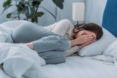 yatakta yatarken, ağlama ve elleriyle yüzünü kaplayan depresif kadın 