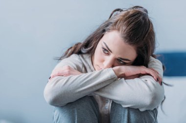 selective focus of beautiful sad woman hugging knees and looking away clipart