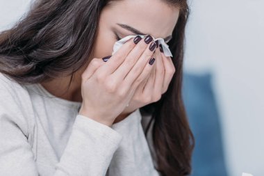 selective focus of grieving woman covering face with hands and crying at home clipart