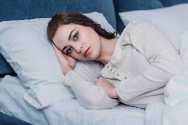güzel üzgün kadın evde yatakta yatan ve kameraya bakarak pijama