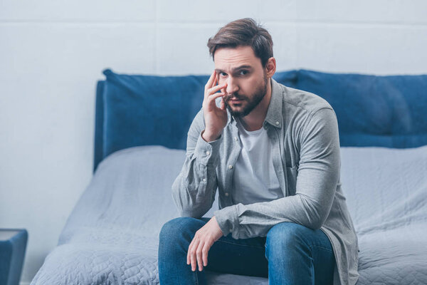 depressed man sitting on bed, looking at camera and grieving at home