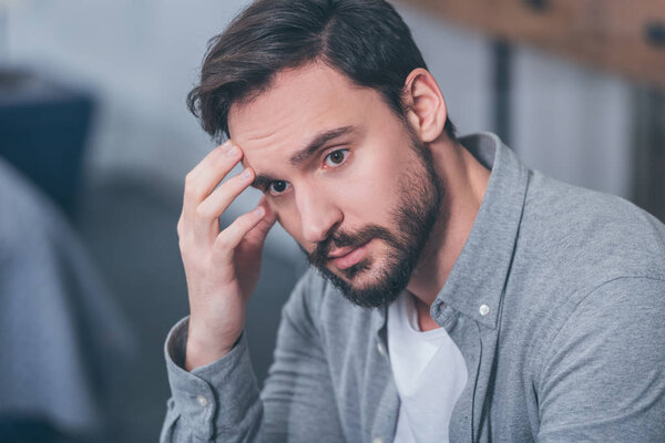 handsome upset man sitting, touching face and grieving at home