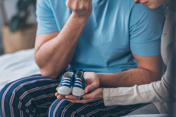 cropped view of parents holding baby shoes at home