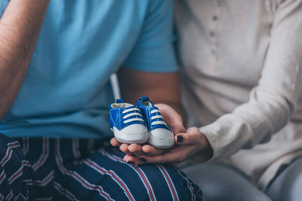 cropped view of parents holding baby shoes at home