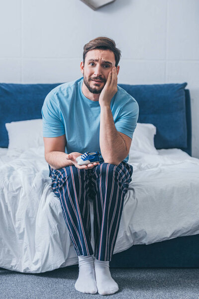 grieving father sitting on bed, looking at camera and holding baby shoe at home