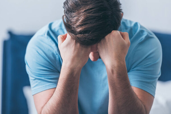 selective focus of grieving man covering face with hands and crying at home